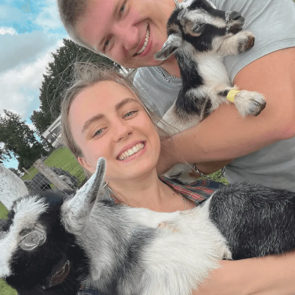 Smiling couple holding baby goats during the Goat Recess experience at Udderly Ridiculous Farm Life.