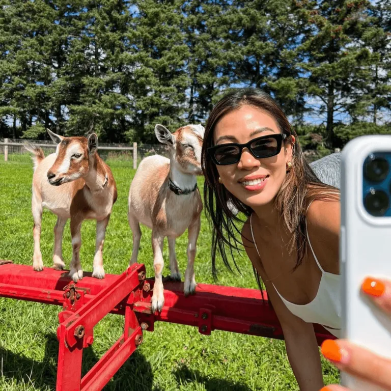 A guest taking a selfie with playful goats during the Goat Recess experience at Udderly Ridiculous Farm Life