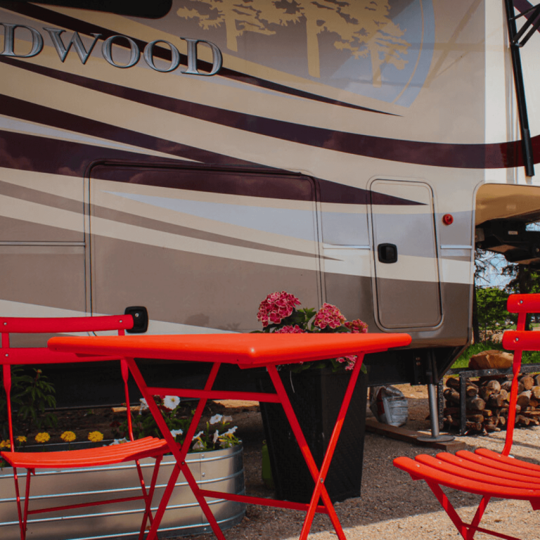 Outdoor seating area with red chairs and table beside RV at Udderly Ridiculous Farm Life.
