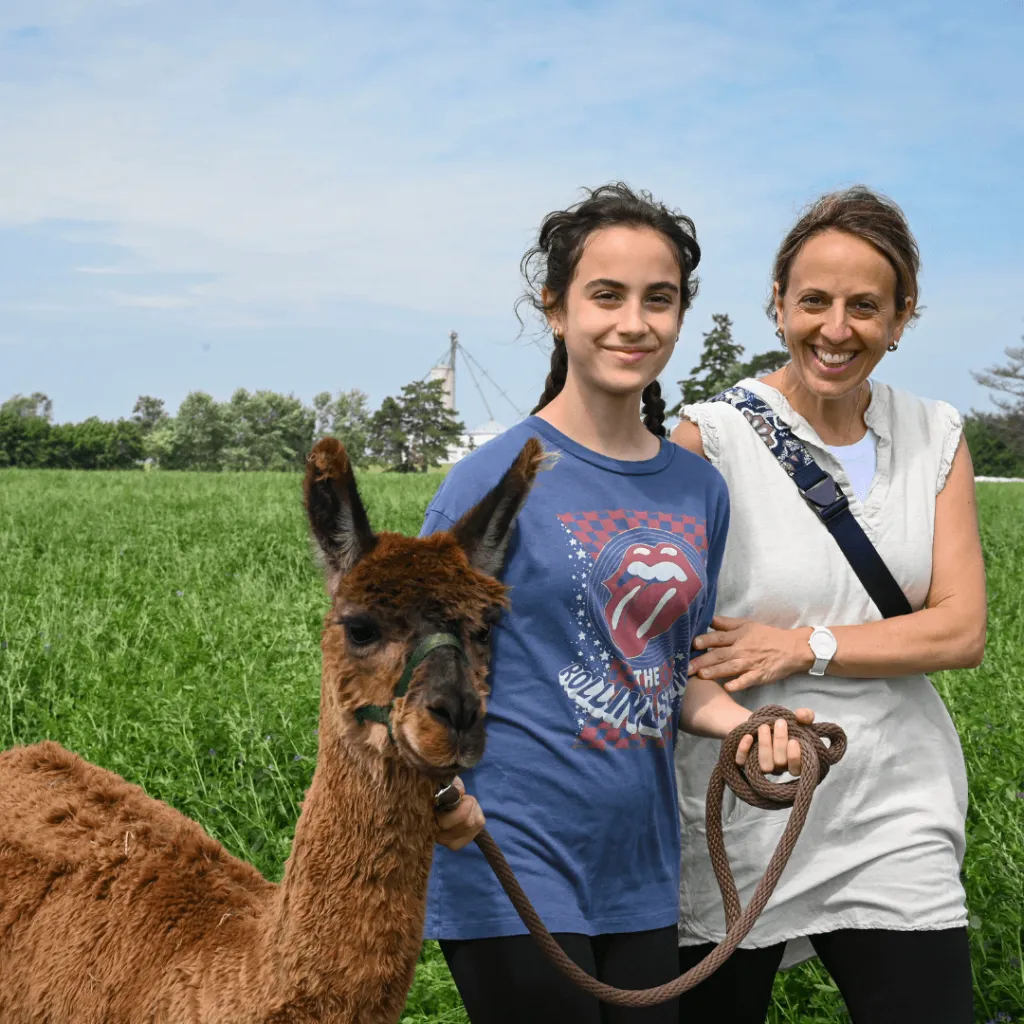 Two guests smiling with an alpaca during the Taste of Farm Life experience at Udderly Ridiculous Farm Life.