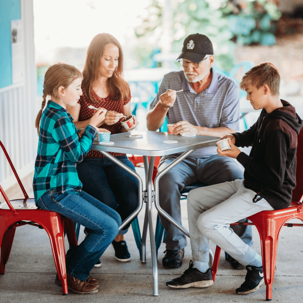 A multi-generational family enjoys artisan goat milk ice cream at an outdoor seating area, sharing a sweet and relaxing moment together.