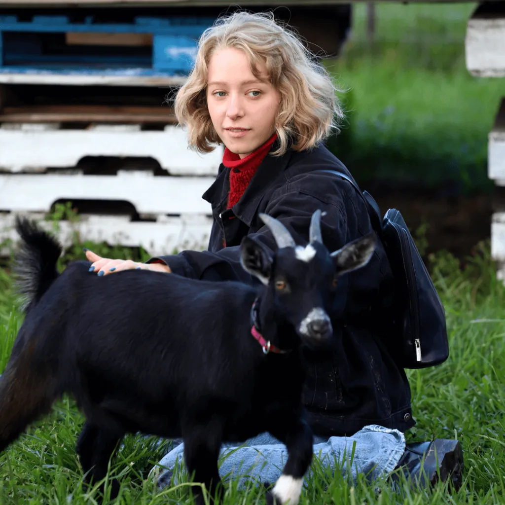 A guest sitting in the grass petting a black goat during the Goat Recess experience at Udderly Ridiculous Farm Life.