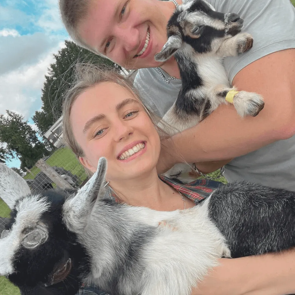 A smiling couple holding baby goats during the Goat Recess experience at Udderly Ridiculous Farm Life.