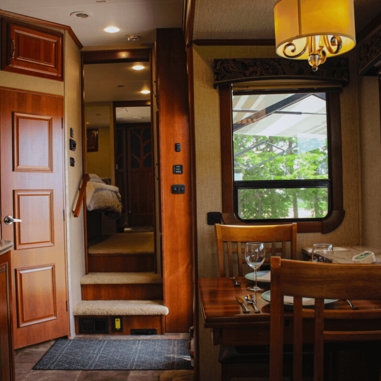 Interior of the luxury RV at Udderly Ridiculous Farm Life, featuring a dining table set for two, stairway to private king bedroom, and ensuite bathroom.