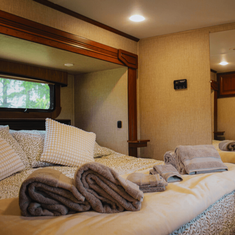 King-size bed in the luxury RV at Udderly Ridiculous Farm Life, neatly made with soft linens, pillows, and rolled towels for the Farm Glamping experience.