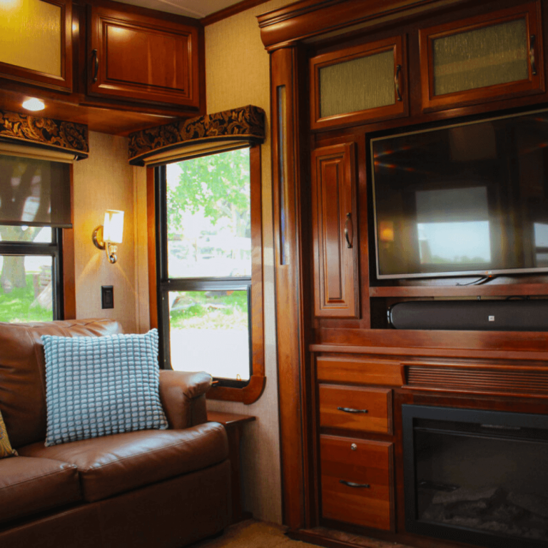Living room inside the luxury RV at Udderly Ridiculous Farm Life, featuring a pull-out sofa, fireplace, TV, and large windows as part of the Farm Glamping experience.