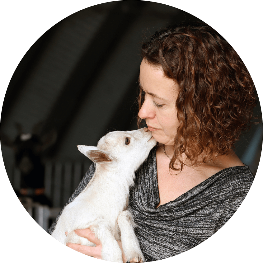 Cheryl Haskett holding a white goat close and smiling softly, founder and CEO of Udderly Ridiculous Farm Life.