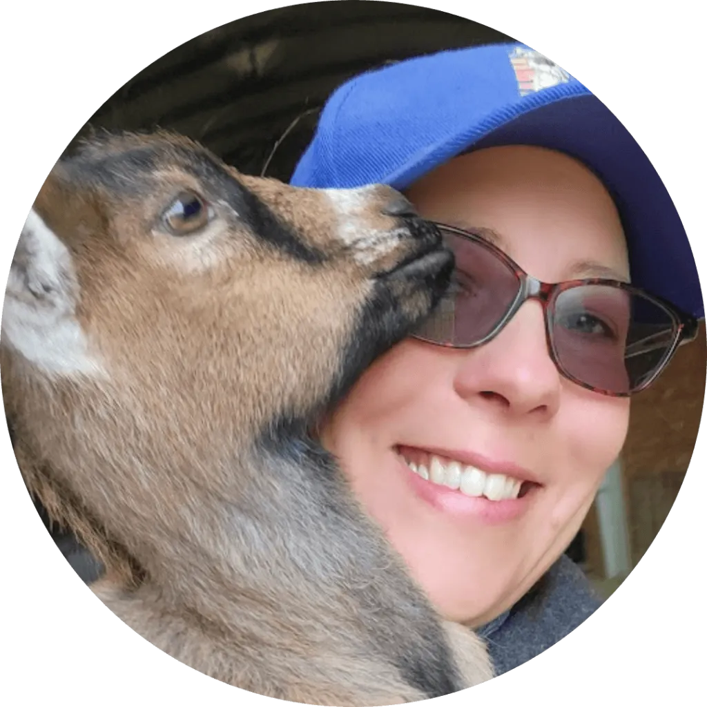 Alexandra Swanson smiling while a goat nuzzles her face at Udderly Ridiculous Farm Life.