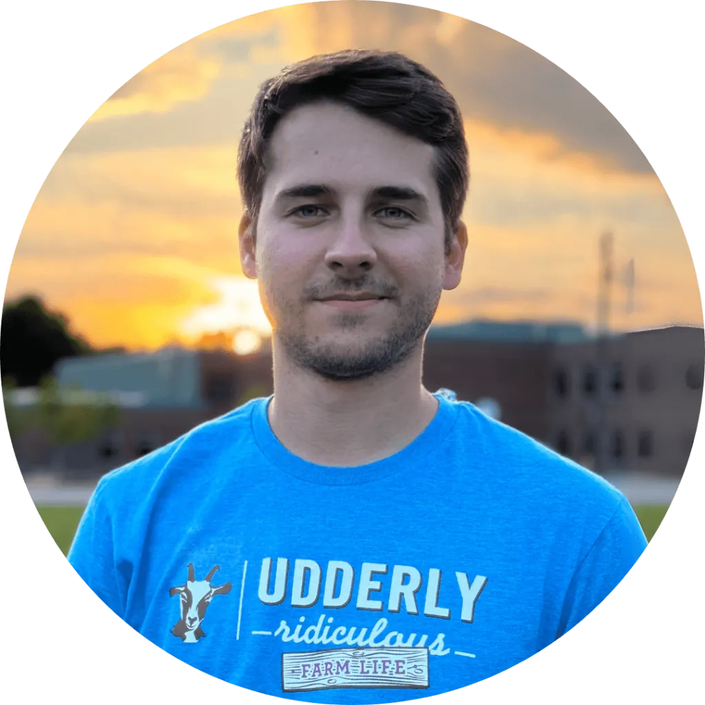 Maxim Axentiev in a blue Udderly Ridiculous t-shirt standing outdoors at sunset.