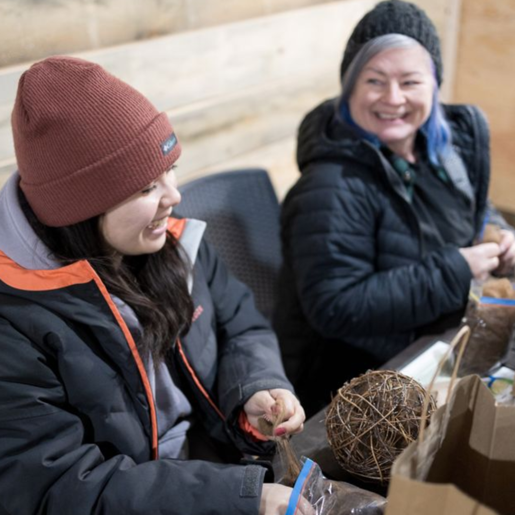 Two women smiling and crafting fibre nesting balls with alpaca fleece during the Alpaca Experience and Fibre Nesting Ball Workshop at Udderly Ridiculous Farm Life.