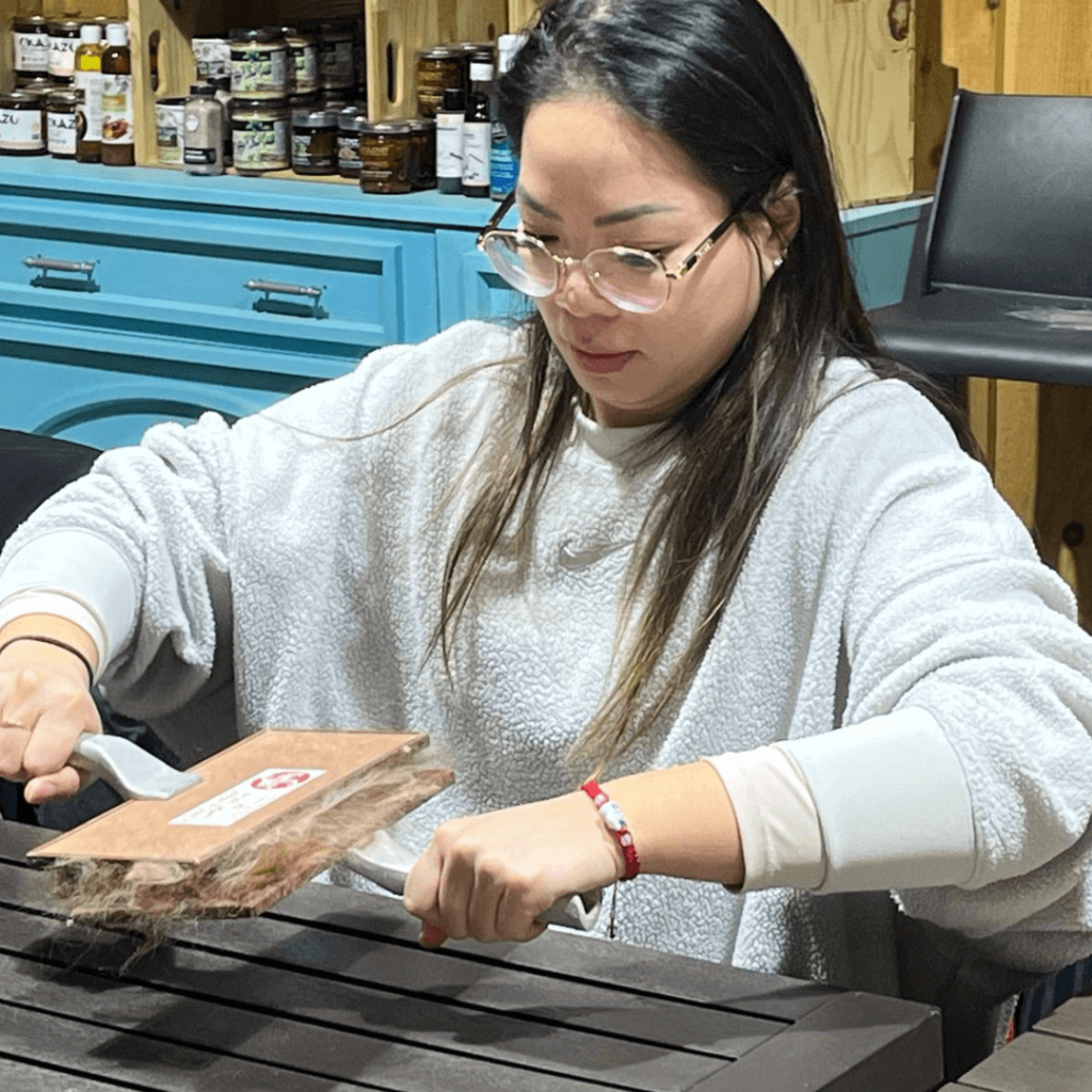 Woman using hand carders to prepare alpaca fleece during the Alpaca Experience and Fibre Nesting Ball Workshop at Udderly Ridiculous Farm Life.