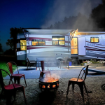 Luxury RV with 4 chairs surrounding a fire during night time